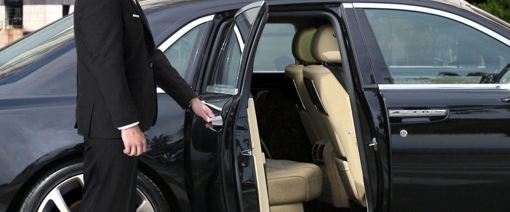 A driver from Prime Limousine Service in Berlin opens the rear door of a black luxury limousine.