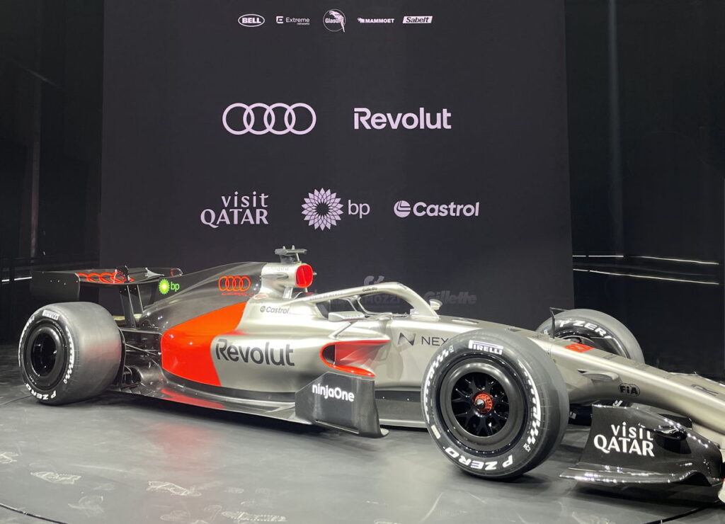 A silver and red Formula 1 racing car from Audi at a presentation.
